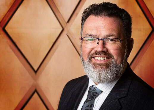 A man standing in front of a wooden wall in suit and glasses